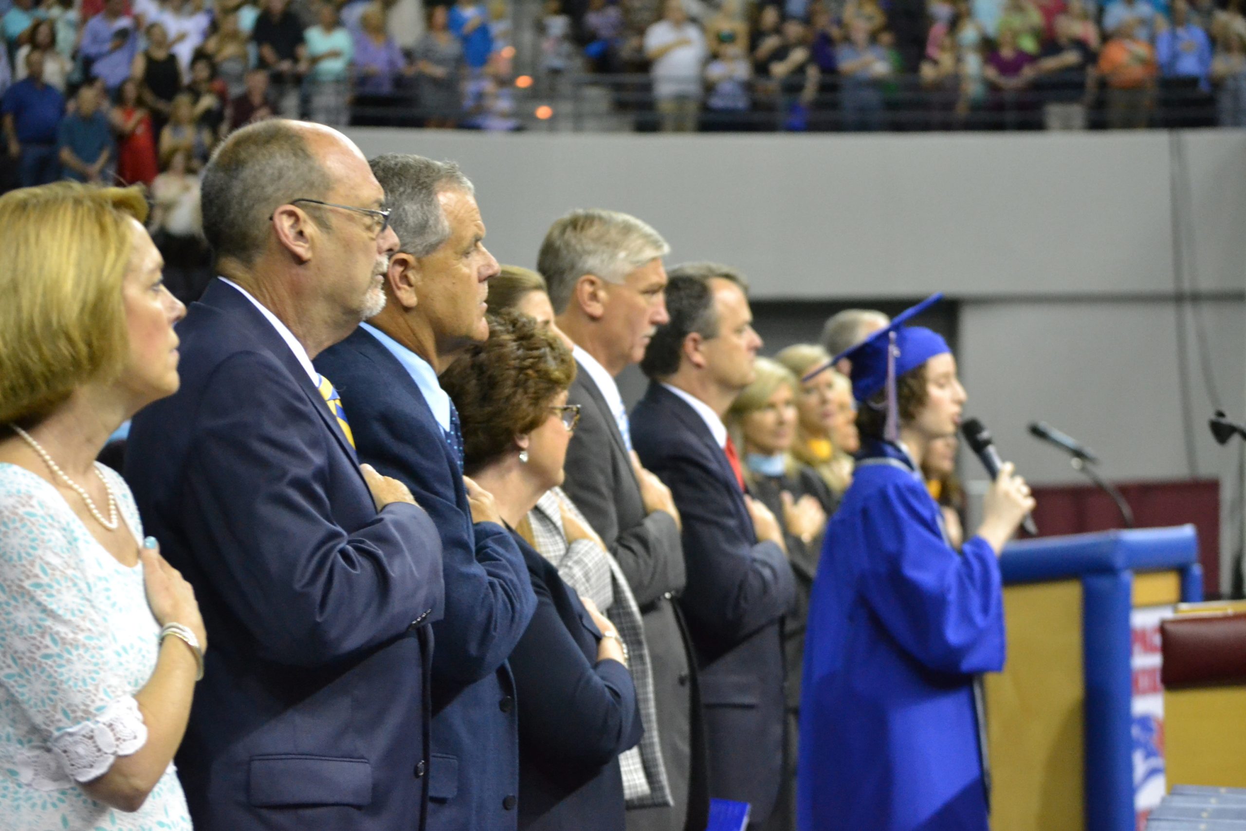 School and district officials stand for the National Anthem, sung by senior Emily Lipford, at Pace High School's May 27 commencement ceremony. [ALICIA ADAMS | Press Gazette]